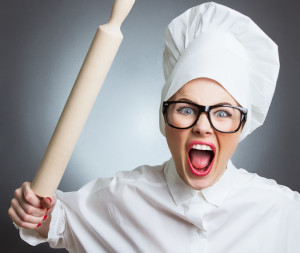 Angry woman cook trying to hit with a rolling pin over a gray background. Funny photo