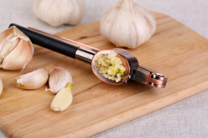 Garlic press on wooden board on light background